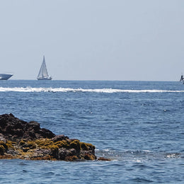 Une image de la mer mediterranee avec un bateau en fond et un rocher devant